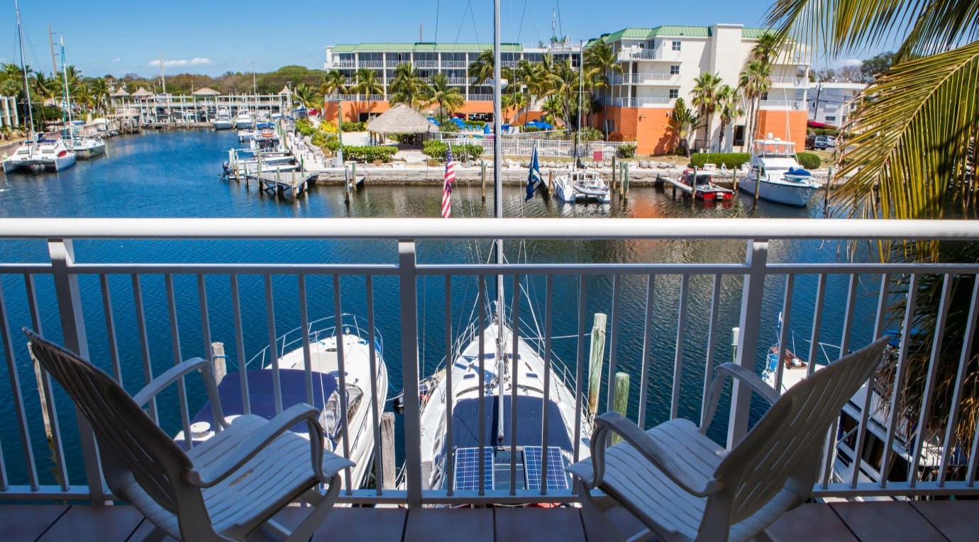 View from a balcony overlooking a marina with boats docked in the water and outdoor seating comprising two chairs facing the water.