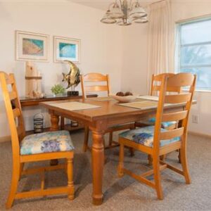 A cozy dining room featuring a wooden table with four chairs, two framed pictures on the wall, and a window with blinds.