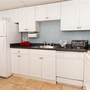 Compact kitchen with white cabinets, appliances, and a red kettle on the counter.